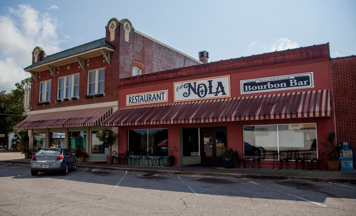 Hotel DeFuniak and Café Nola frontage with restaurant signage and striped awnings