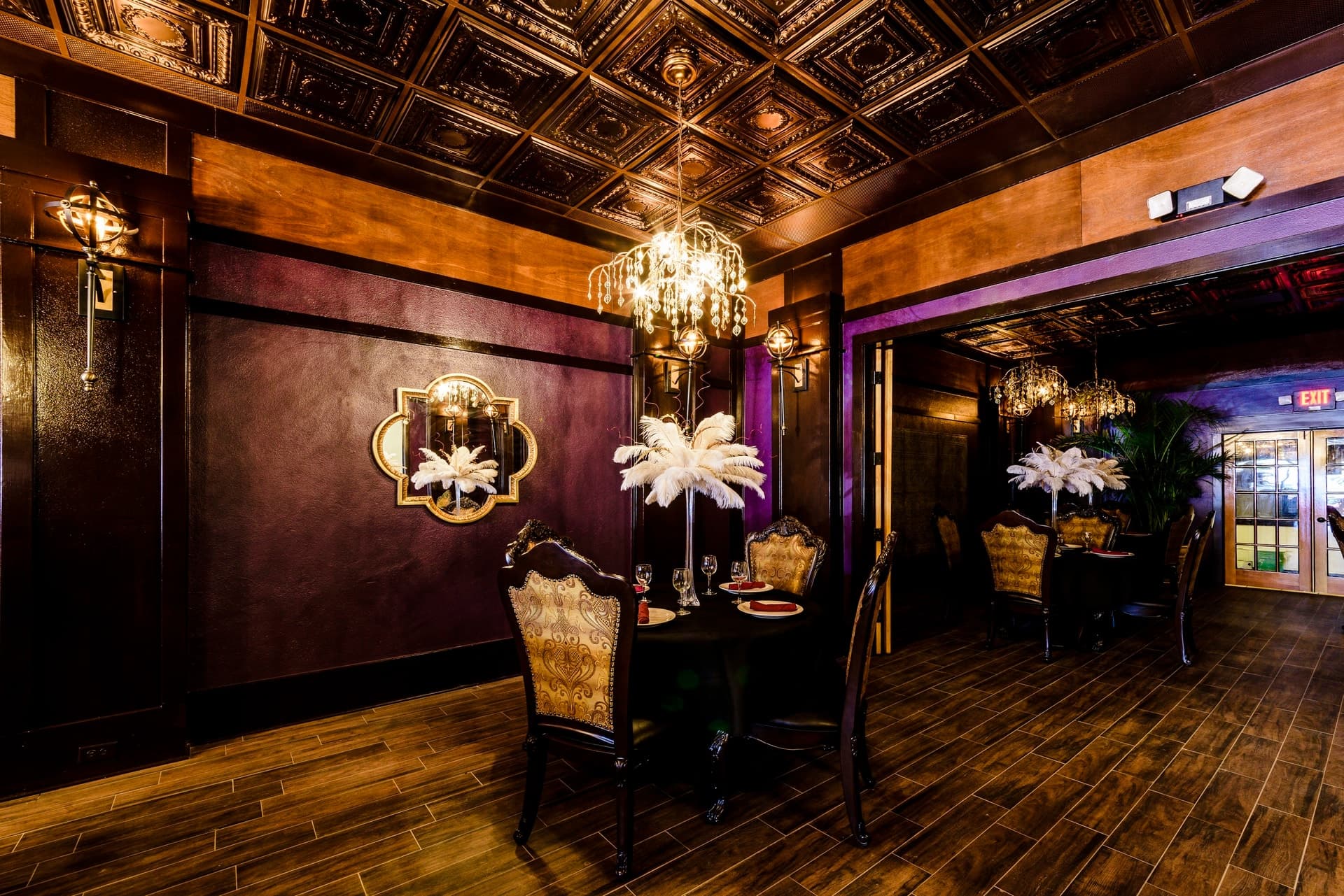 Café Nola dining room with chandeliers, upholstered chairs and a patterned ceiling